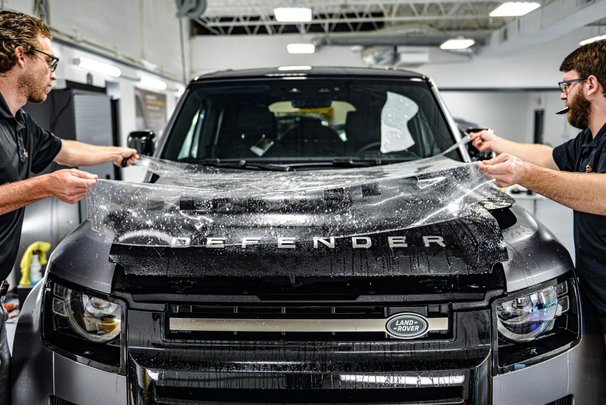 two technicians installing paint protection film to a black land rover defender